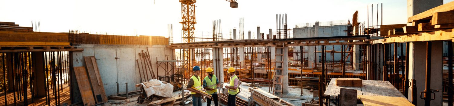 Construction industry concept - architects and engineers discussing work progress between concrete walls, scaffolds and cranes.